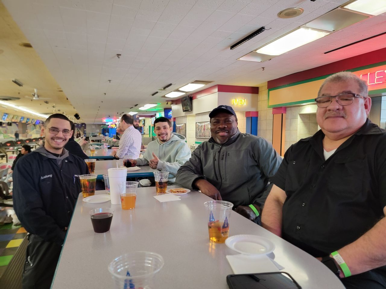 Four people seated at a table in a bright indoor restaurant, smiling with drinks and cups nearby.