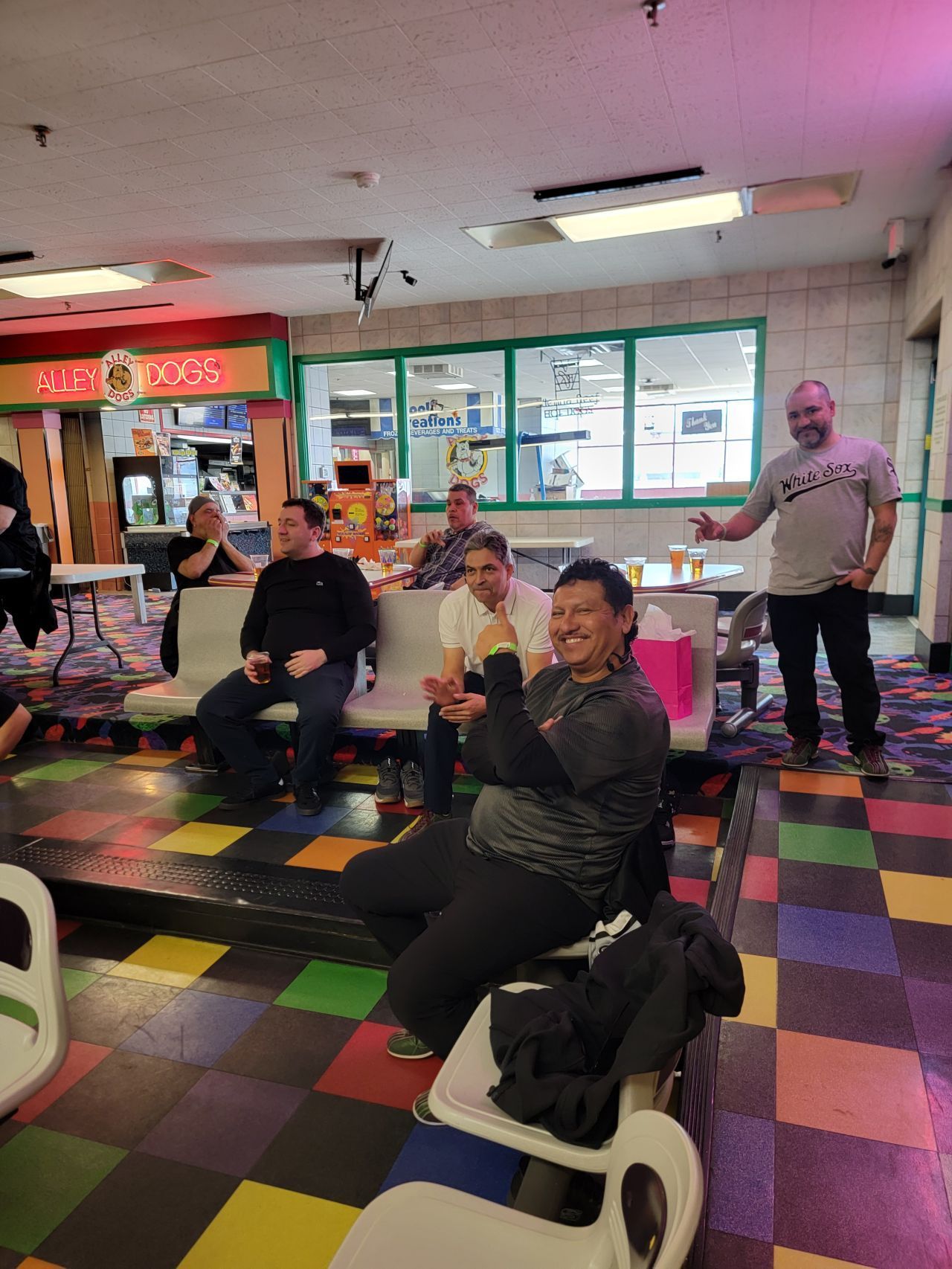 People sitting and standing in a colorful indoor arcade, one man clapping near the front.