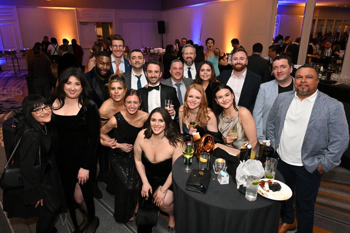 Group of people posing at a formal indoor party with purple lighting and a cocktail table