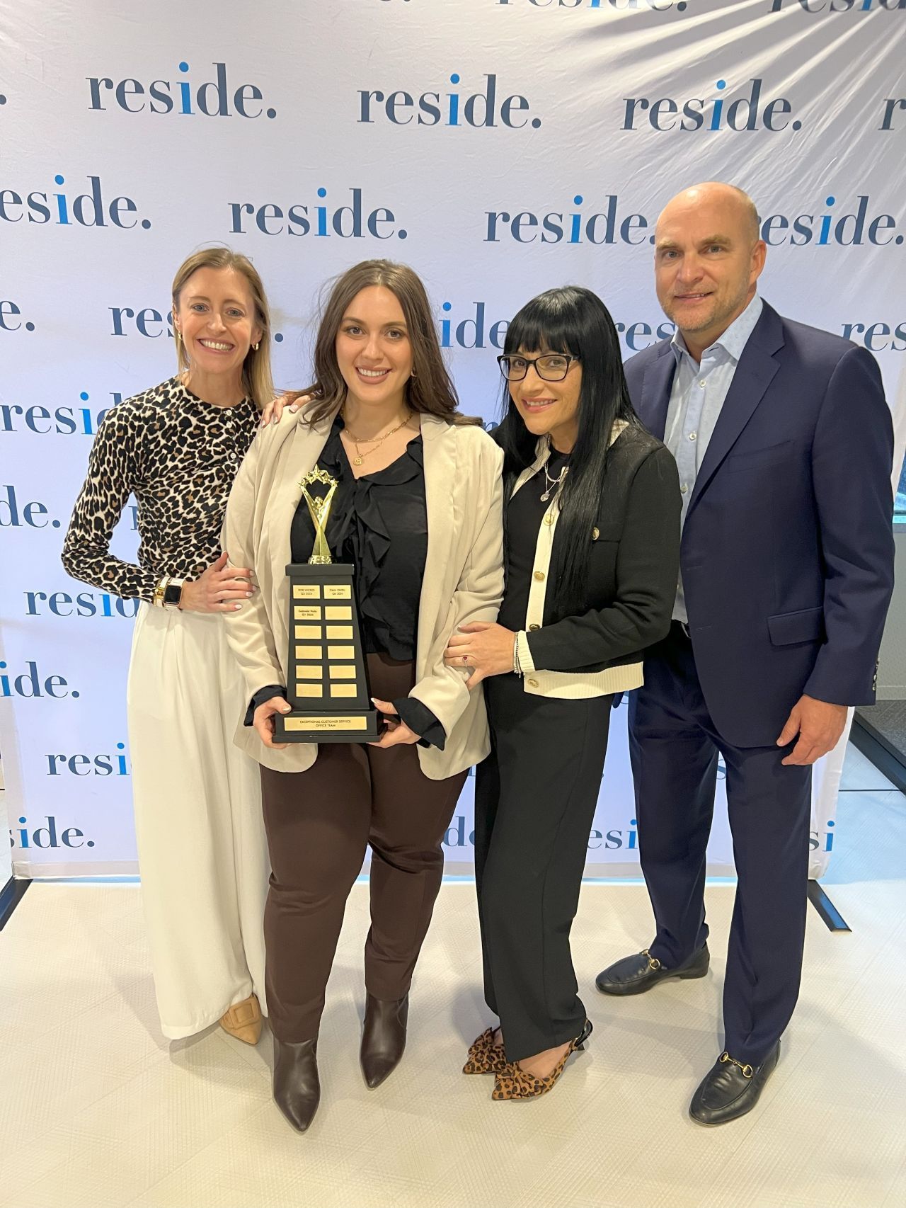 Four people posing with a trophy at a Reside event backdrop