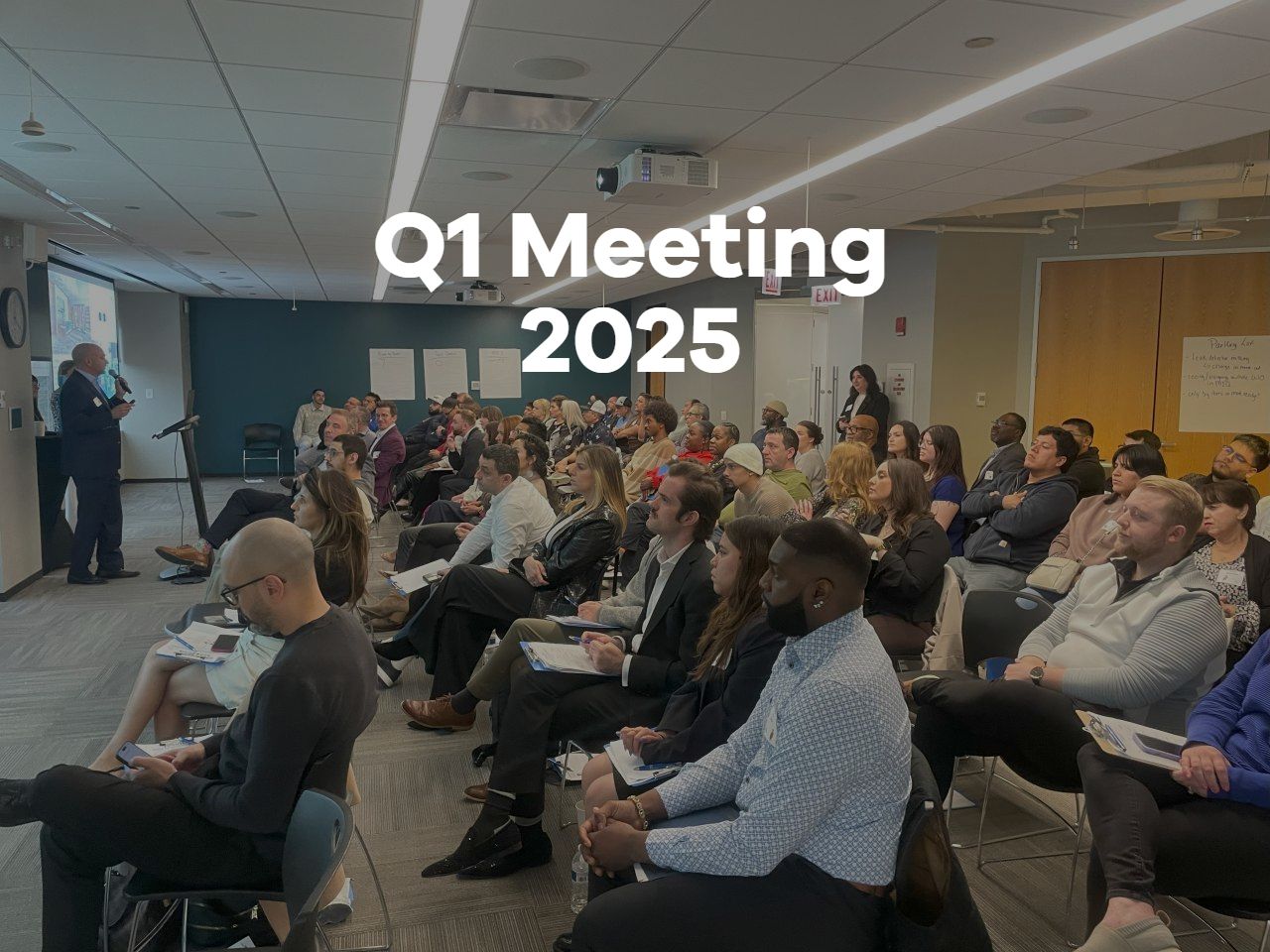 Q1 Meeting 2025 with a seated audience in a conference room, watching a speaker at the front