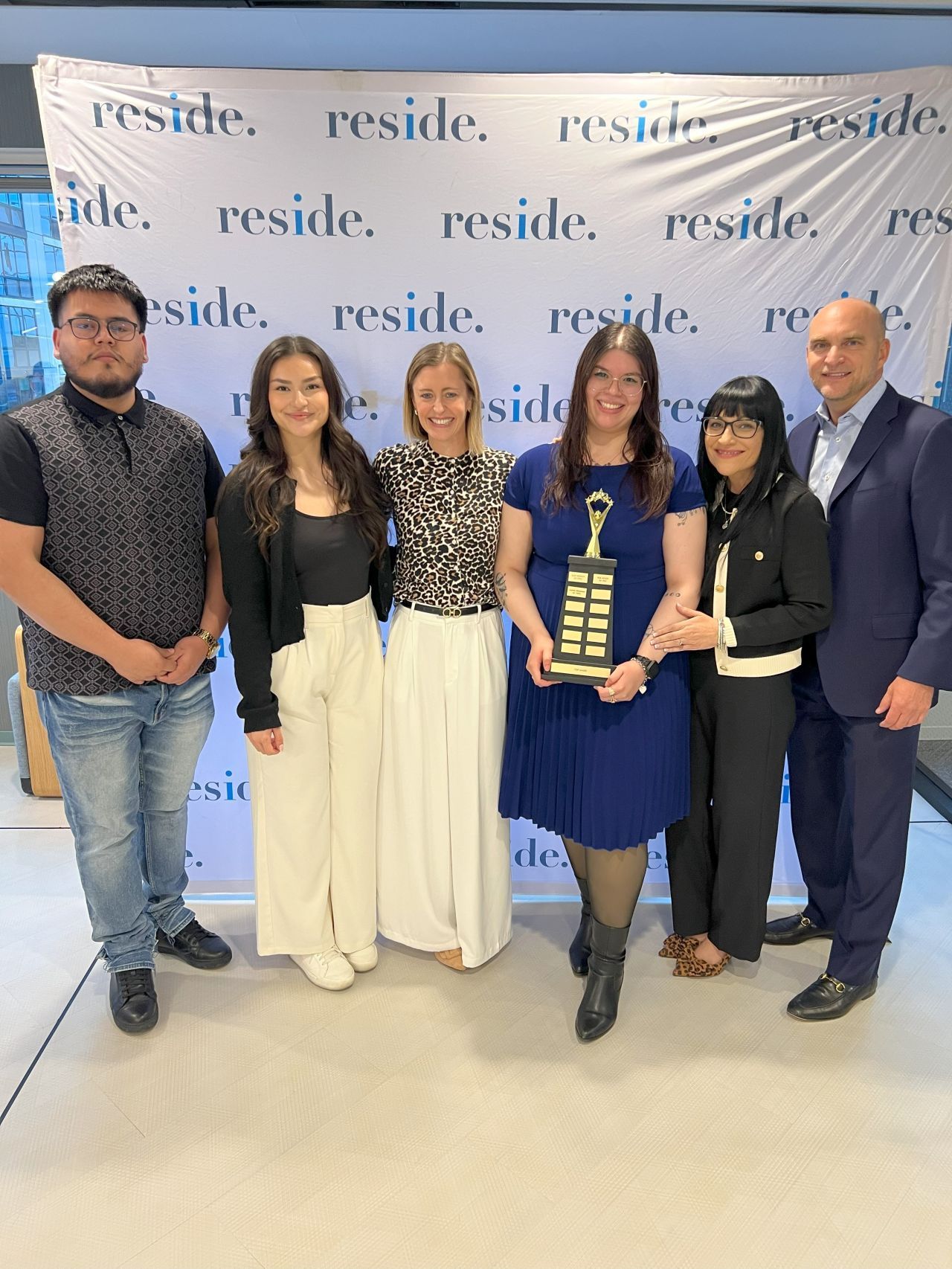 Six people posing with an award plaque in front of a 