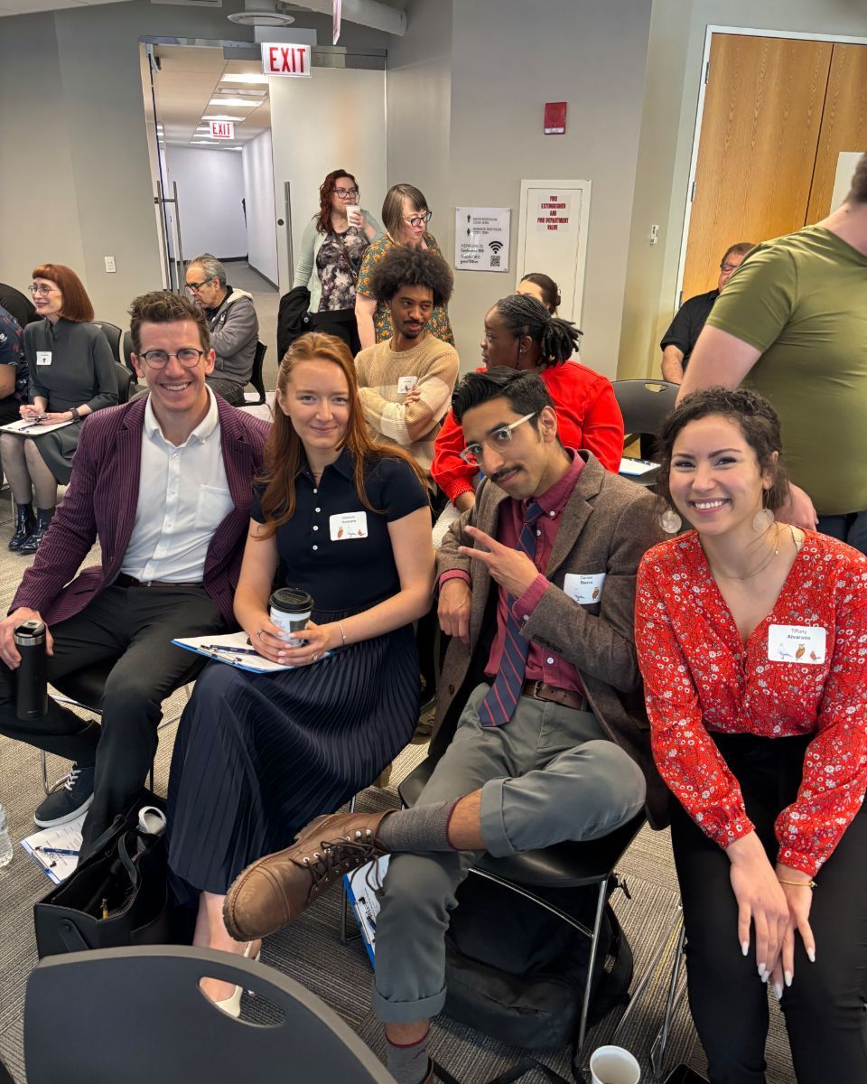 Conference attendees seated in a hallway, smiling and posing for a group photo.