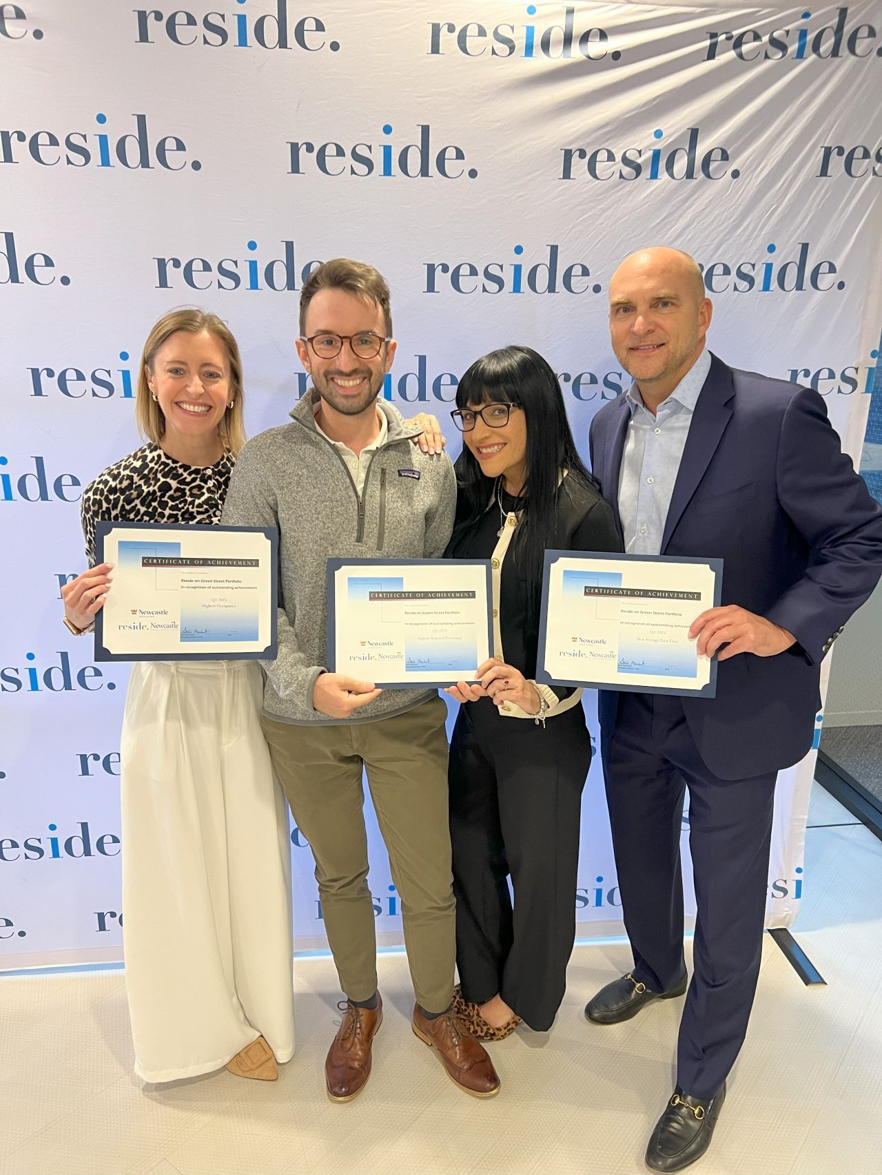 Four people holding certificates stand in front of a repeating 