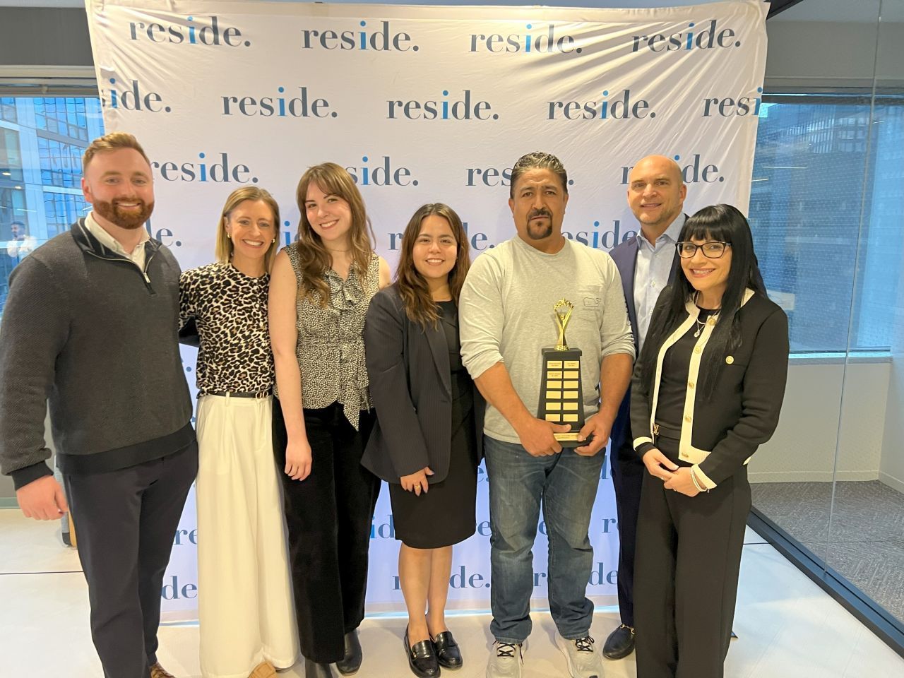 Six people posing with an award in front of a branded backdrop at an indoor event