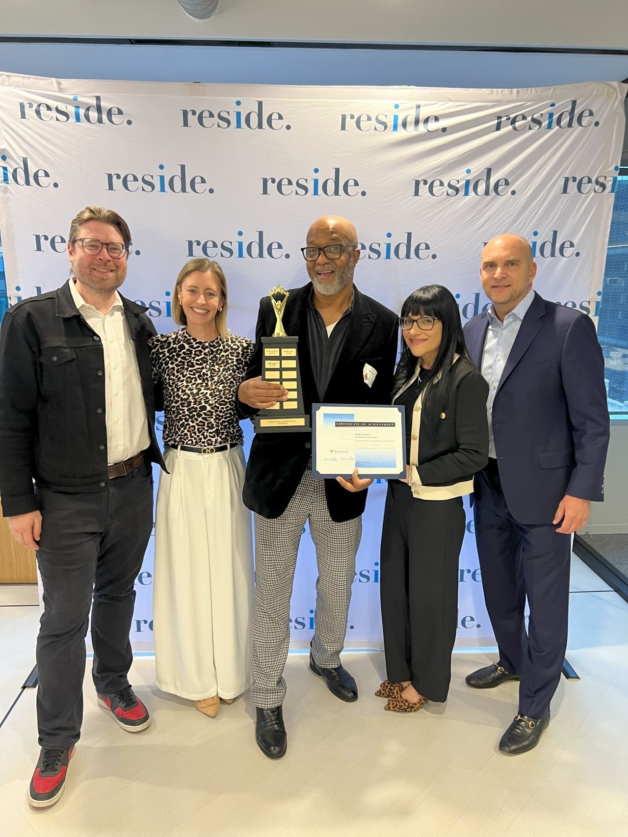 Five people posing at a conference backdrop, two holding an award certificate and plaque.