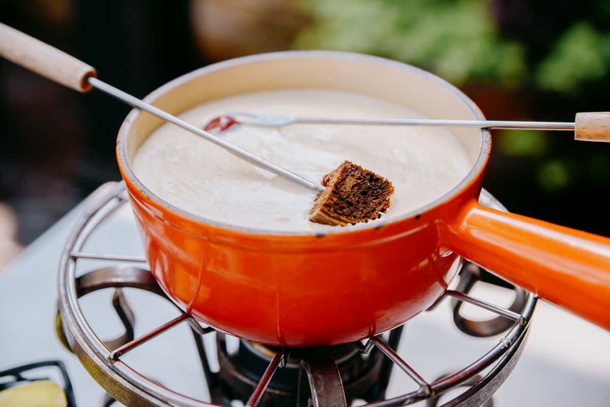 A person is dipping a piece of meat into a pot of fondue.