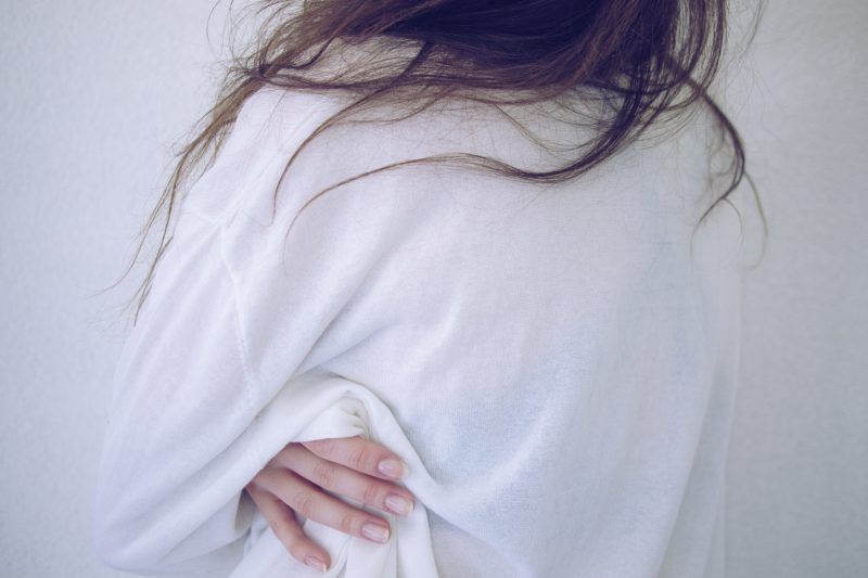 A woman is wearing a white shirt with her hands behind her back.