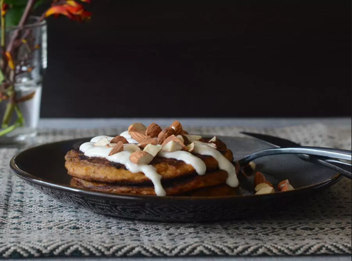 A stack of pancakes with nuts and whipped cream on a plate with a fork