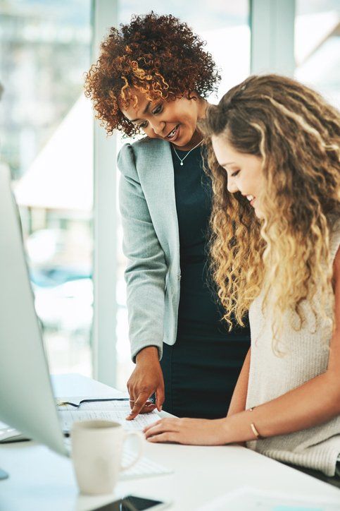 Two women are looking at a computer screen together in an office.