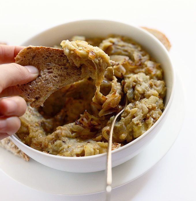 A person is holding a piece of bread over a bowl of food