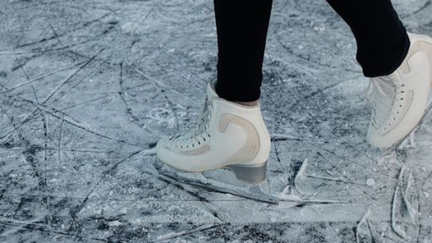 A close shot of a girl ice skating on the ice with black legging and white ice skate shoes.