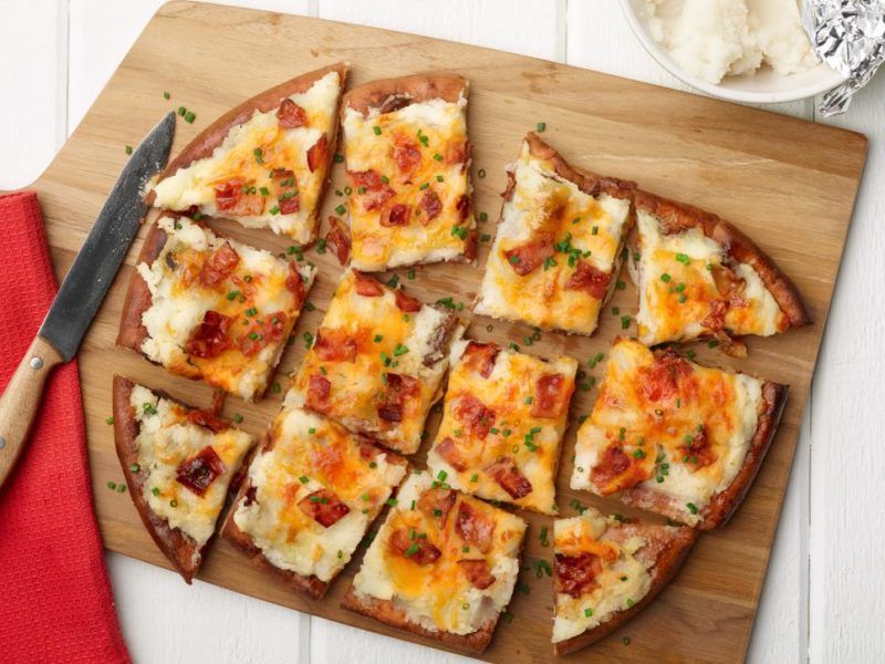 A pizza with bacon and cheese is sitting on a wooden cutting board.