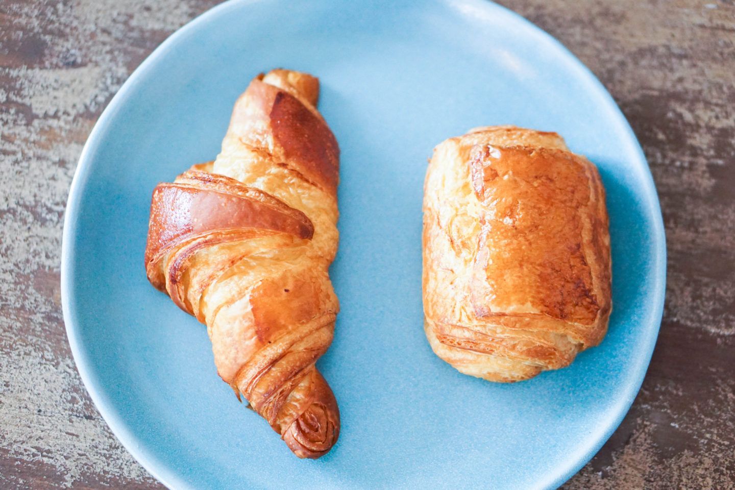 A croissant and a chocolate cake are on a blue plate.
