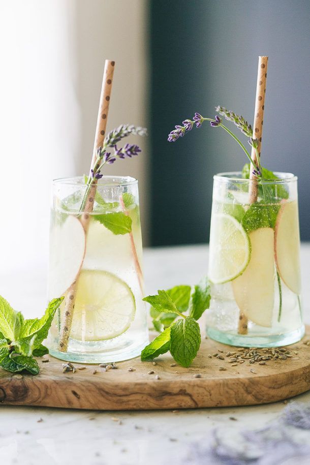 Two glasses of lemonade with straws on a wooden cutting board.