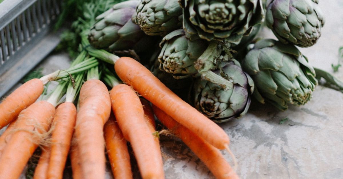 A bunch of carrots and artichokes are sitting on a table.