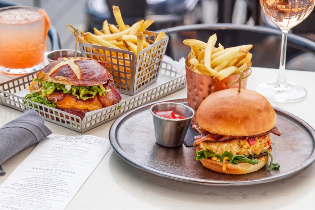 A table topped with hamburgers and french fries and a glass of wine.