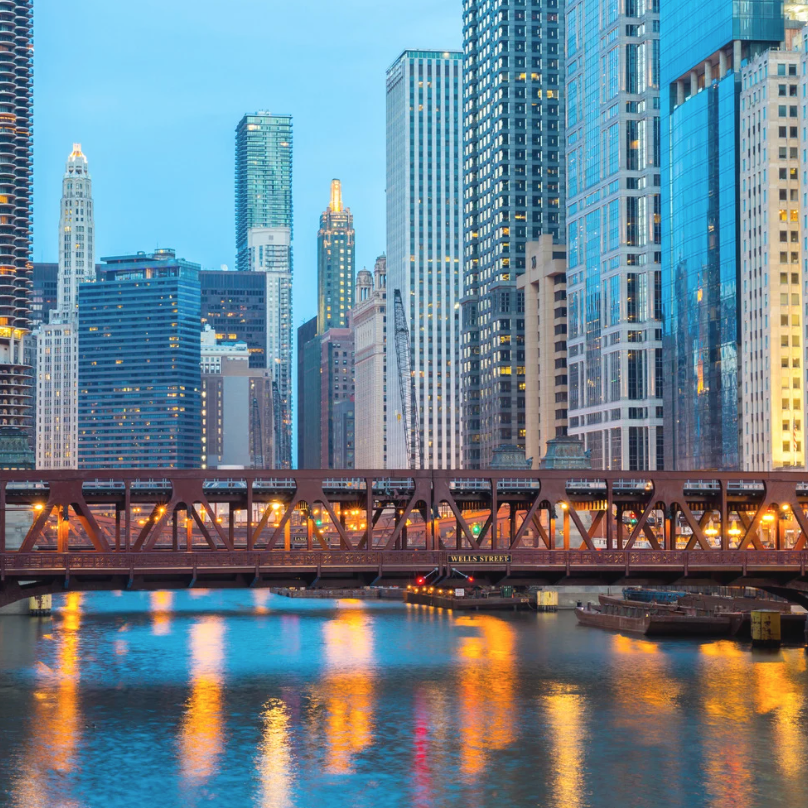 Chicago skyline with bridge over water reflecting city lights.