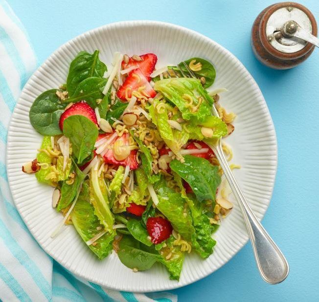 A white plate topped with a salad with strawberries and lettuce