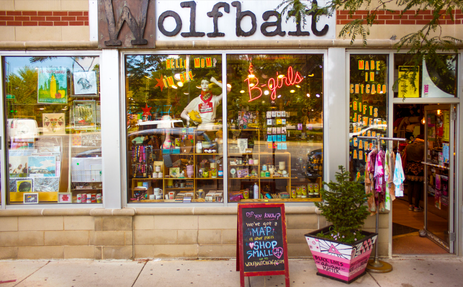 The Wolfbait store storefront with merchandise in the windows, a pink-painted planter, and a sidewalk sign.