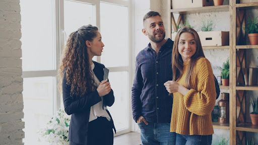 Three people standing and talking in a bright office with shelves and plants in the background