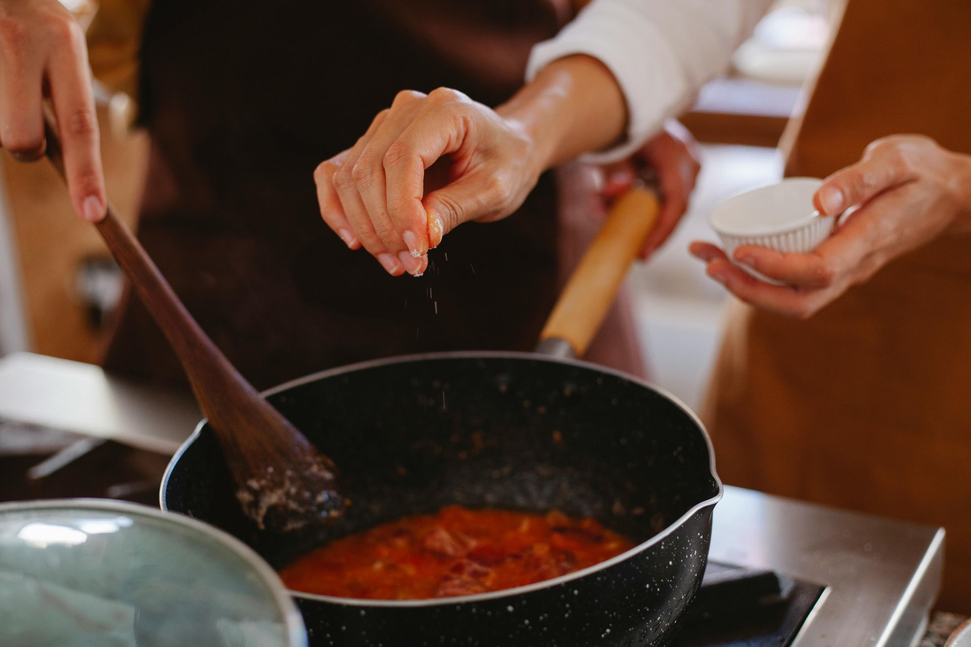 A close-up shot of two people cooking, with one person’s hand seasoning the food in the pot.
