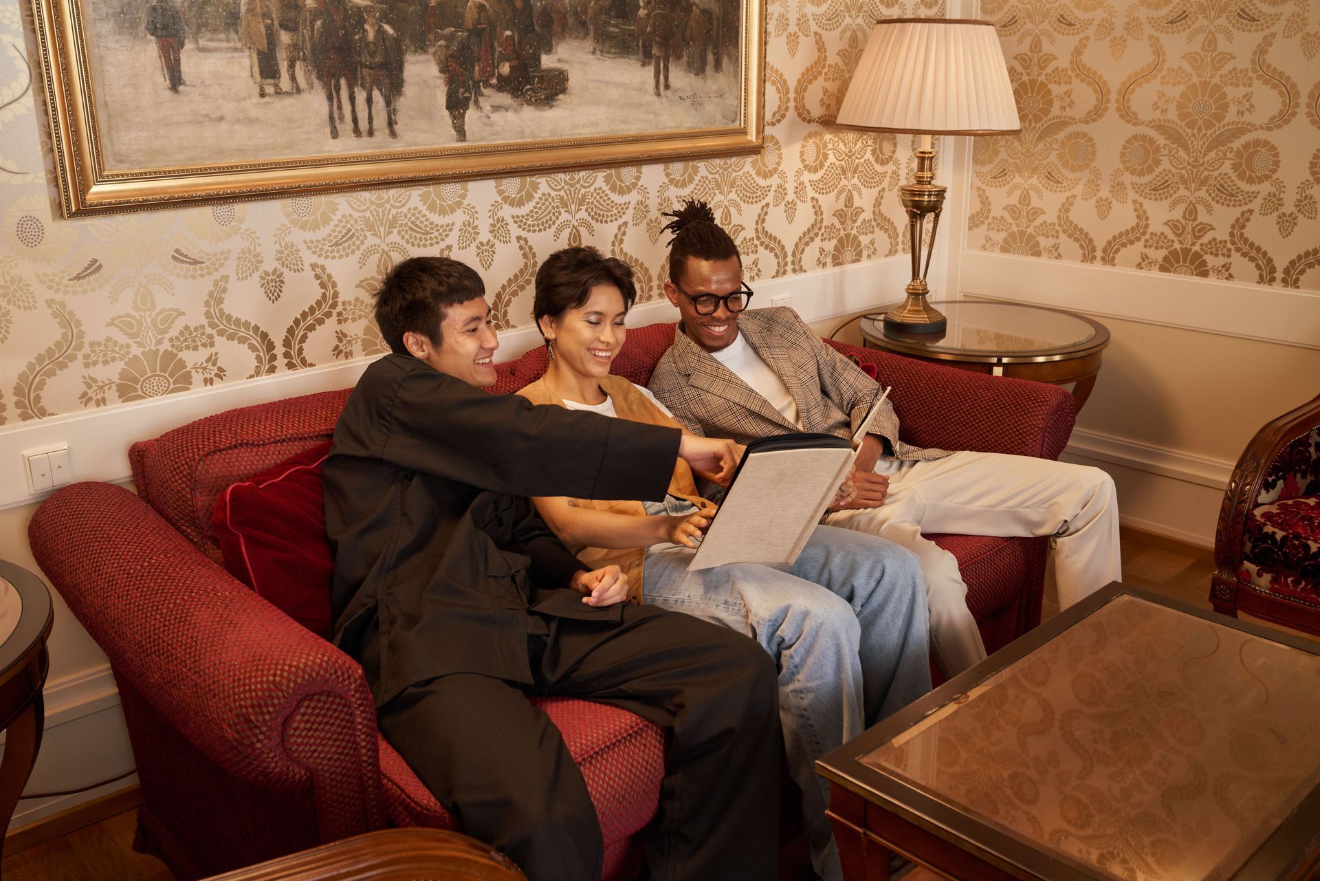 Three people sit on a red couch in a living room, looking at something offscreen.
