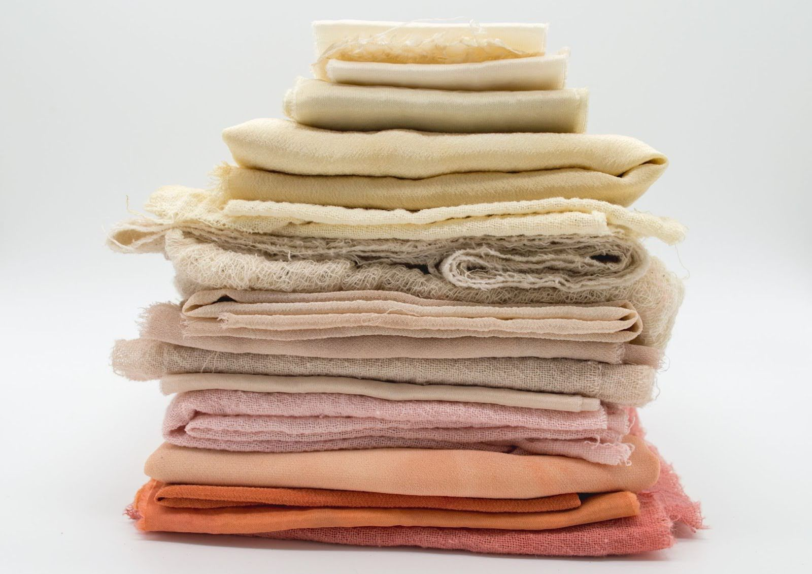 Stack of folded textile and fabrics in colors grading from light orange to warm brown earth tones