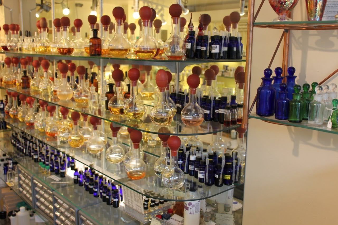 Glass shelves filled with rows of round perfume bottles with atomizers and small blue and green apothecary vials.