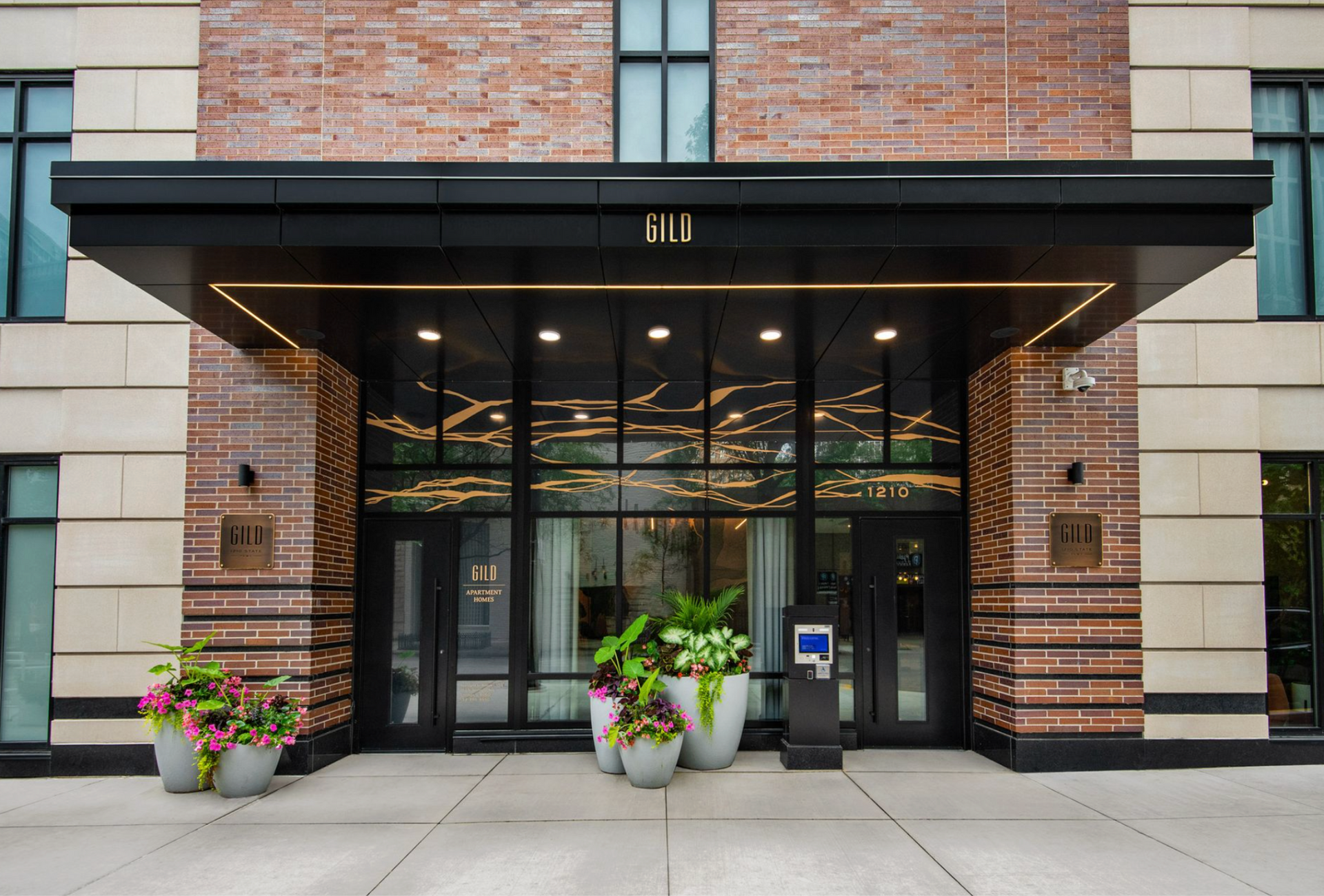 Modern brick building entrance with glass doors, potted flowers, and black awning