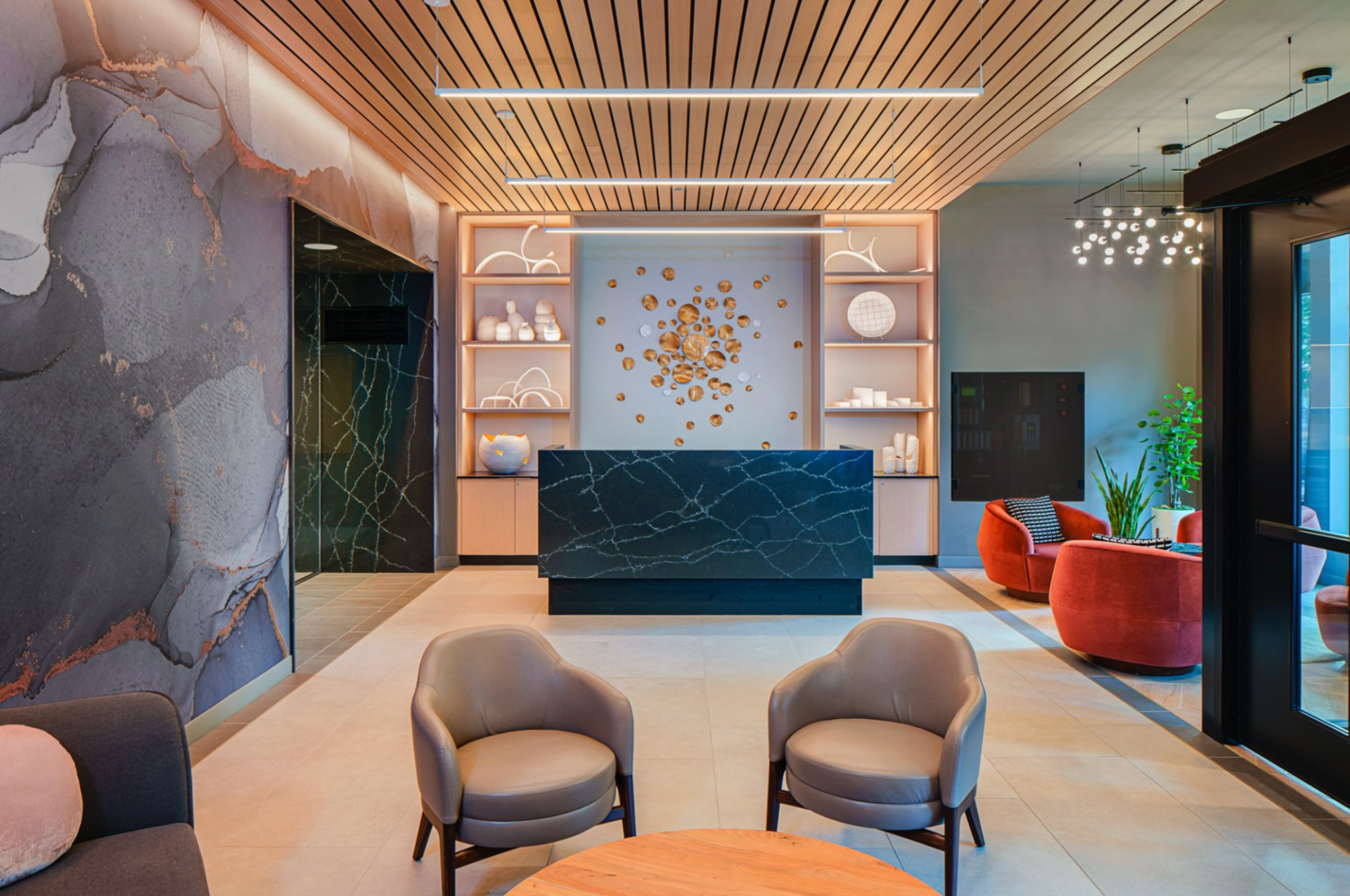 Modern hotel lobby with marble walls, blue reception desk, lounge chairs, and warm ceiling lighting