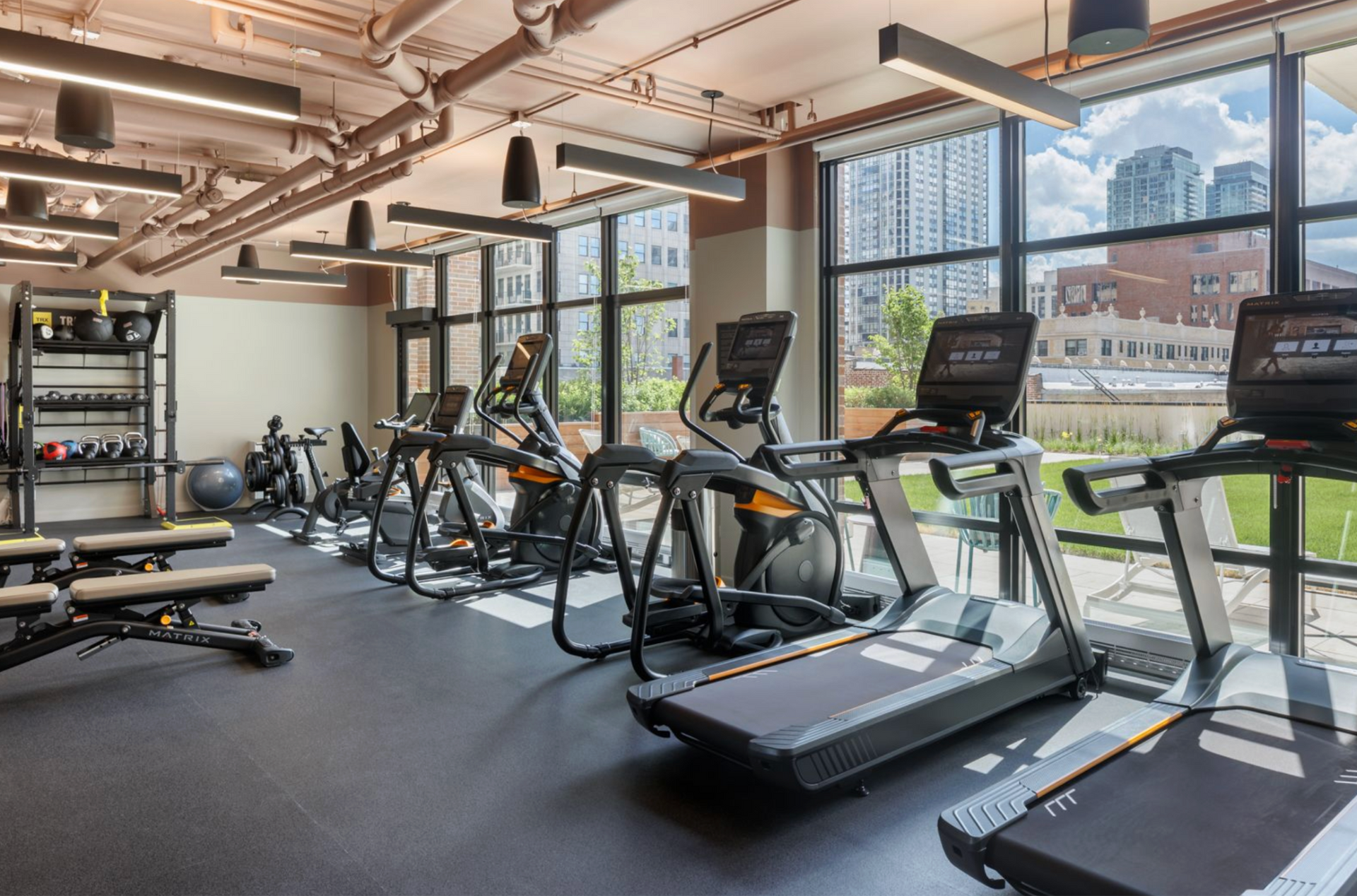 Modern gym with treadmills, ellipticals, and large windows overlooking a city view