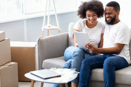 Couple on a couch looking at papers in a bright living room, with moving boxes nearby