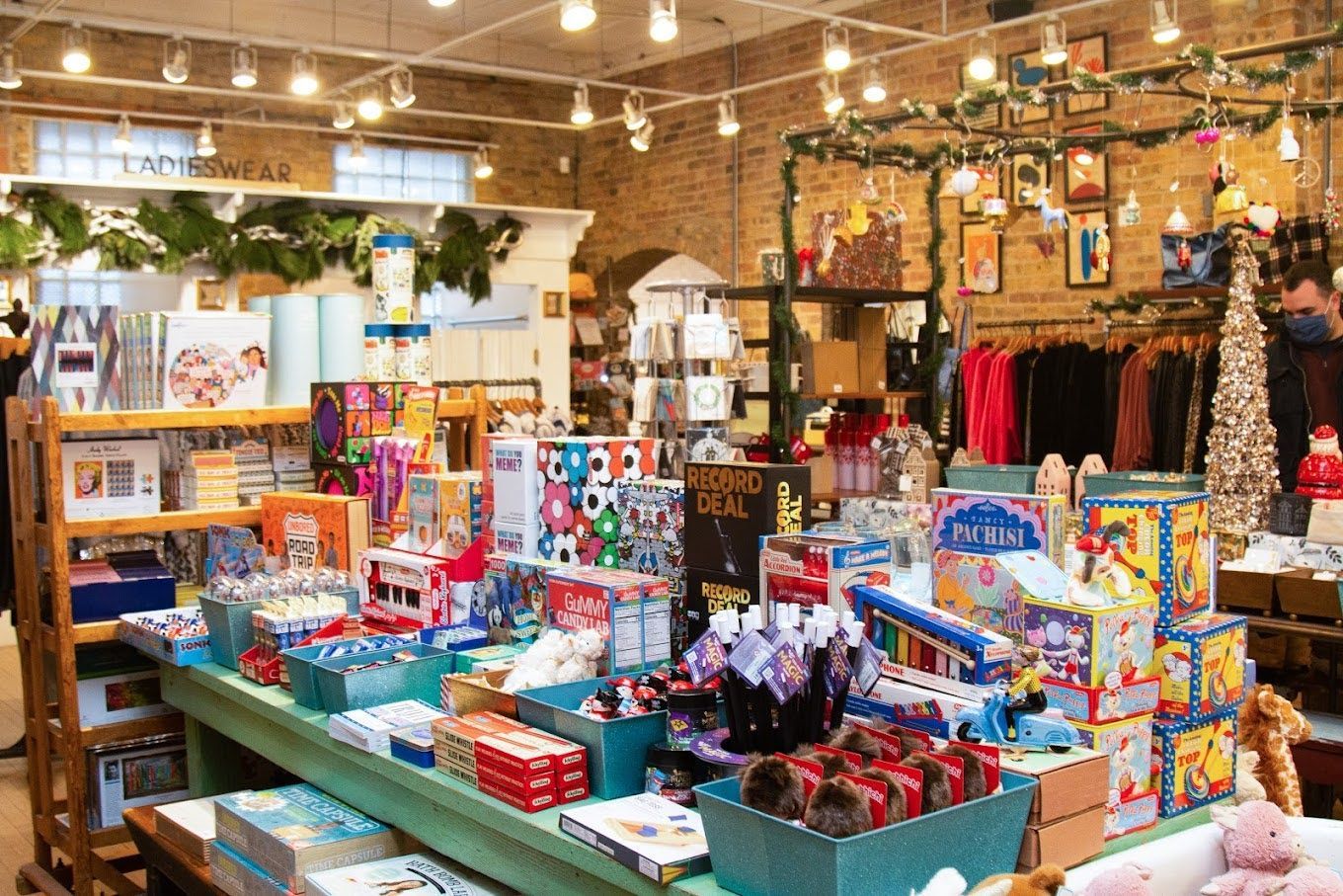 A retail shop filled with colorful toys and gifts displayed on tables and shelves with rustic brick walls and warm lighting.