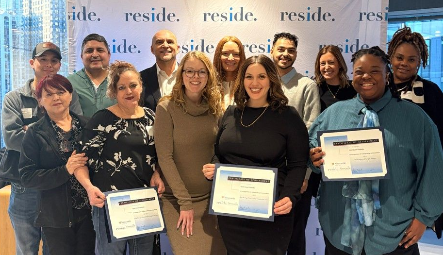 Group of people posing with certificates at a residence-branded event, smiling indoors.