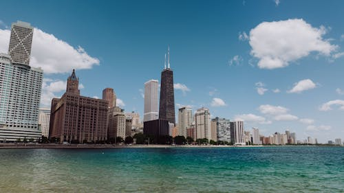 City skyline with tall buildings along turquoise water under a partly cloudy blue sky