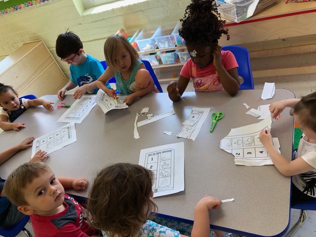 Children doing a paper craft activity around a table in a classroom
