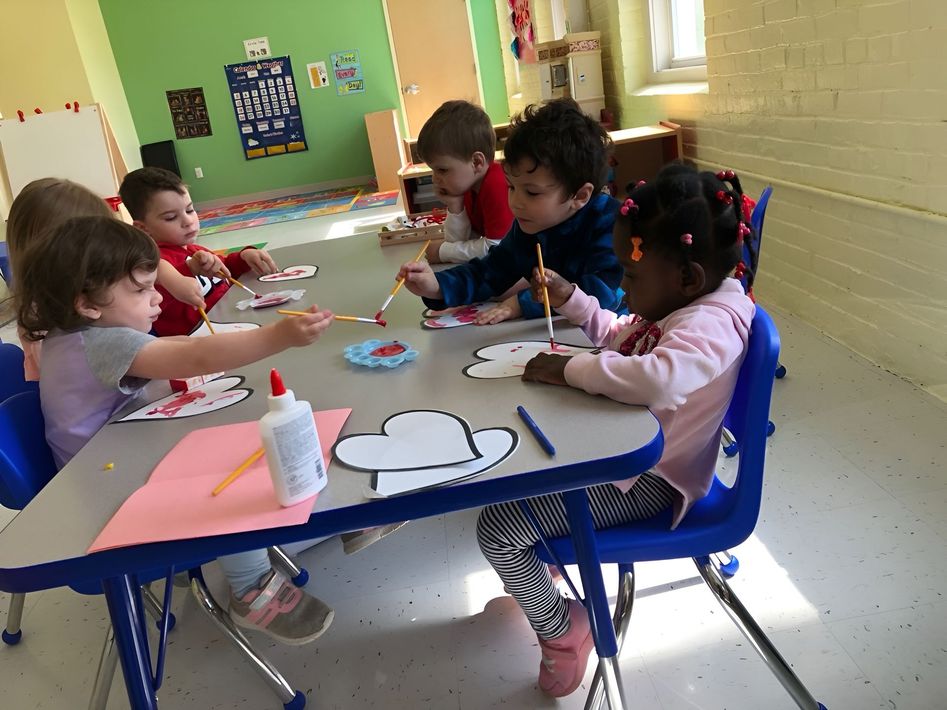 Children seated at a classroom table doing arts and crafts with paper and markers