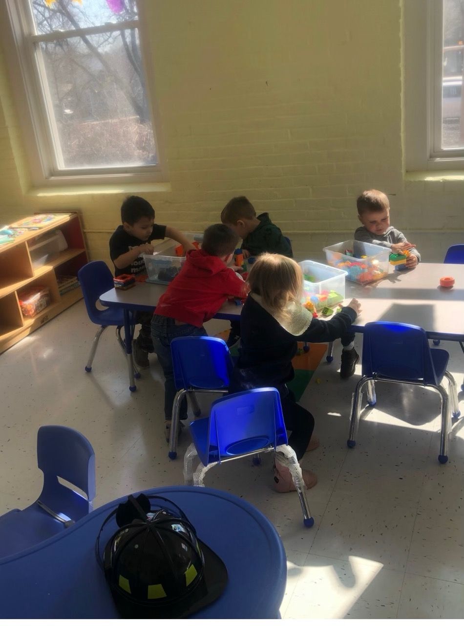 Children seated around a table doing crafts in a bright classroom