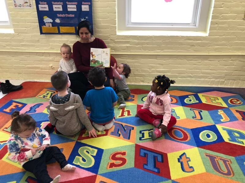 Teacher reading to children on a colorful alphabet rug in a classroom
