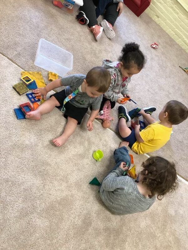 Children playing with toy cars on a carpeted floor in a classroom.