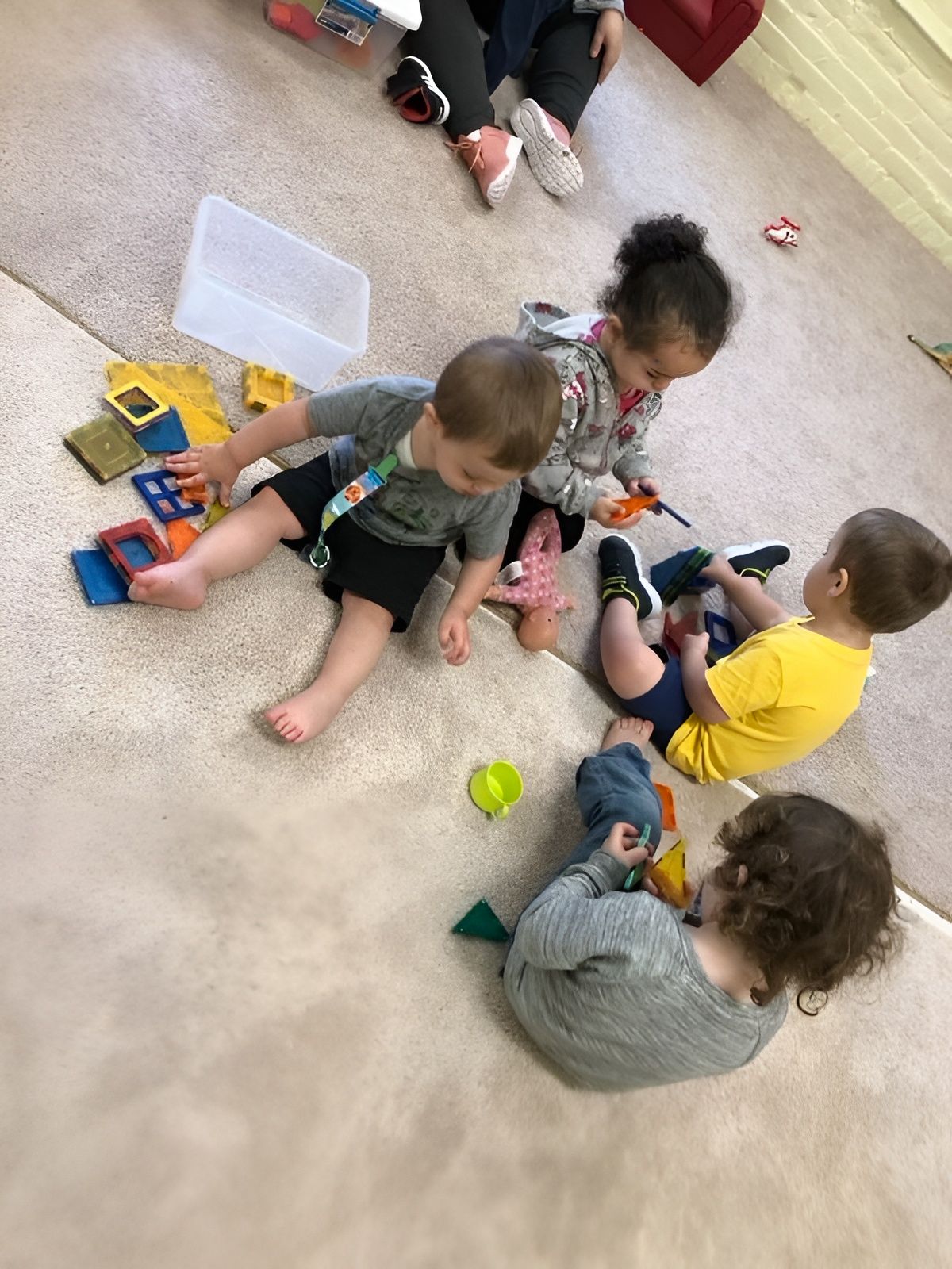 Children playing with toys on a carpeted floor in a classroom.