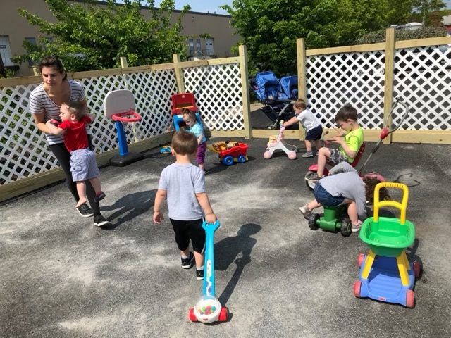 Children playing with toys in a fenced outdoor yard on a sunny day