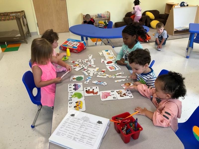 Children seated around a classroom table using picture cards and crayons during a group activity