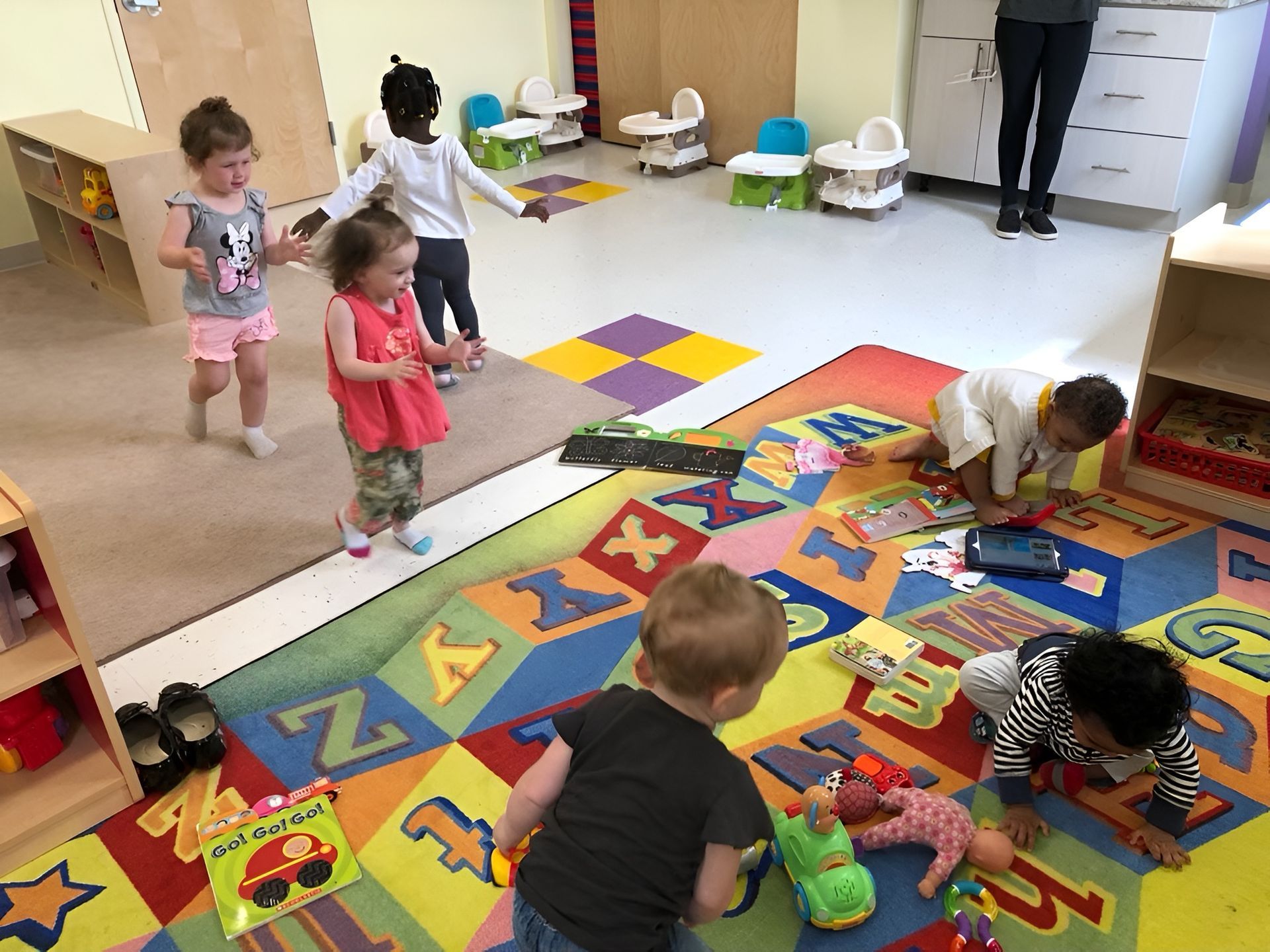Children playing with toys on a colorful classroom rug in a daycare room