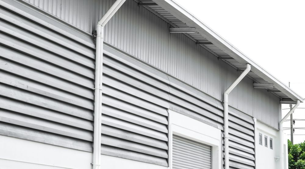 Gray industrial building with horizontal siding and rain gutters.