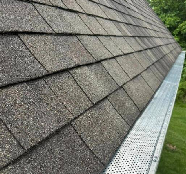 Close-up of a roof with gray asphalt shingles and a metal gutter with a leaf guard.