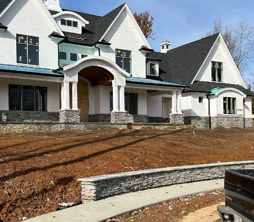 White house under construction with stone accents, brown soil, and blue trim.