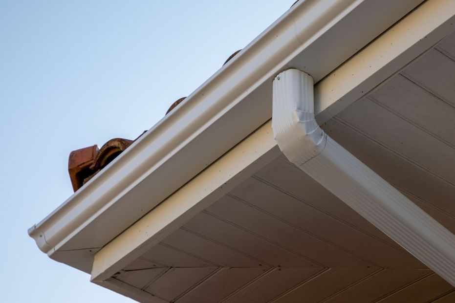 White gutters and downspout on a house with a tan soffit and red tile roof.