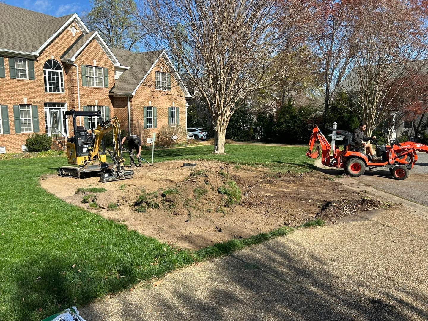 Suburban yard work with two orange tractors digging a large dirt patch beside a brick house